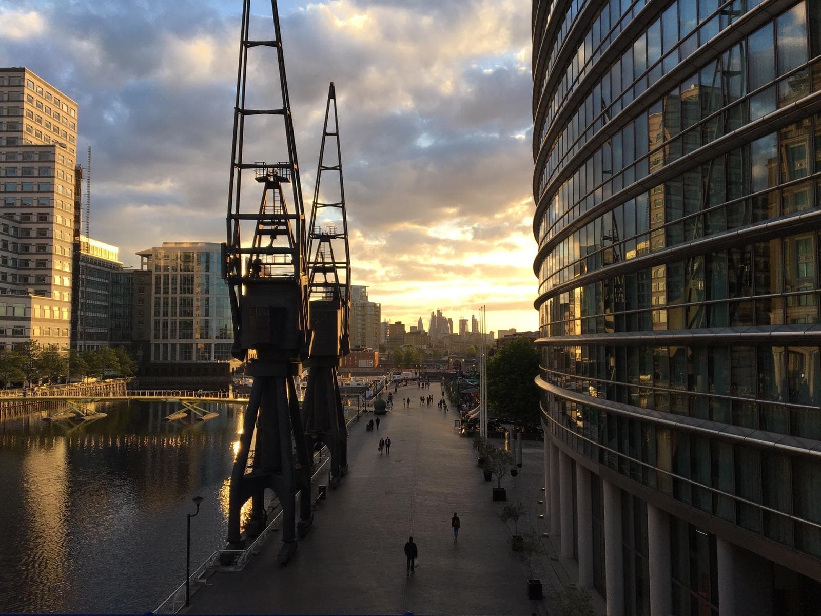 Canary Wharf waterfront in London at sunset, with glass office towers and a dockside crane
